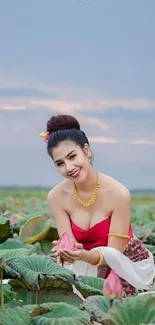 Woman in traditional attire amidst lotus field in serene setting.