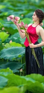 Woman in a red top holding lotus flowers surrounded by green leaves.