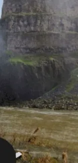 Misty waterfall with cliffs and river landscape.