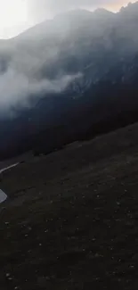 Serene misty mountain road with dark cloudy sky.