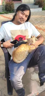 A man comfortably seated with a cat on his lap outdoors.