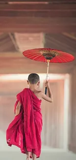 Monk in a red robe holding an umbrella, walking in a calm corridor.