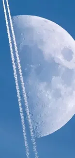 Half moon with vapor trails in a blue sky.