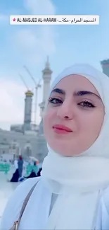 Woman in white hijab at Al-Masjid Al-Haram, blue sky background.