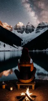 Campfire under a starry sky by mountains and lake.