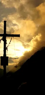 Silhouette of a mountain cross at sunset with orange and yellow hues.