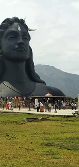 Large statue with mountain backdrop and lush green field.