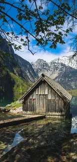 Rustic cabin by a tranquil mountain lake with snowy peaks.