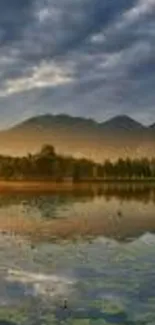 Serene lake at sunset with mountains and a cloudy sky.