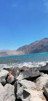 Serene mountain lake with rocky shoreline under a clear blue sky.