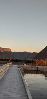 Serene view of a wooden dock leading into a mountain lake under a light brown sky.