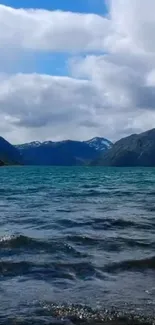 Serene lake with mountains under cloudy sky.