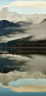 Mountain lake with misty reflection and snowy peaks.