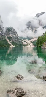 A tranquil mountain lake with clear green water surrounded by misty peaks and forests.