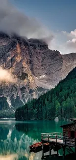 Serene mountain lake with forest and cabin under clouds.