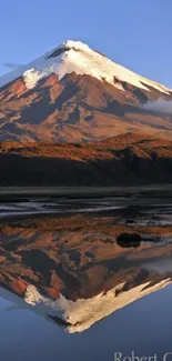 Snow-capped mountain reflected in calm lake at sunset.