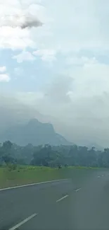 Misty mountain road with lush greenery and cloudy sky.