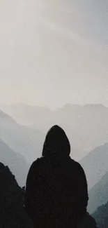 Silhouette of person with mountain ranges in the background under a bright sky.