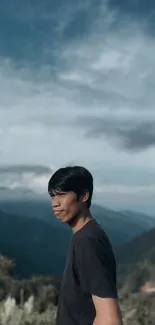 Person in black shirt with mountain and sky background.