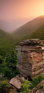 Sunset over a lush green mountain valley with a prominent rock formation.