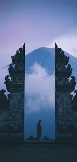 Man standing in temple gate with mountain backdrop at dusk.