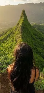 Woman gazing at lush green mountain ridge under a serene sunset.