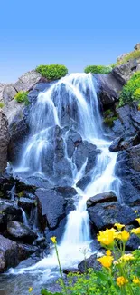 Serene mountain waterfall with blue sky and wildflowers.