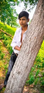 A young man leaning against a tree in a lush green forest.