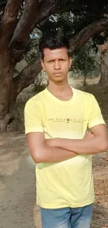 Person in yellow shirt walks through lush, green trees on a sunny day.