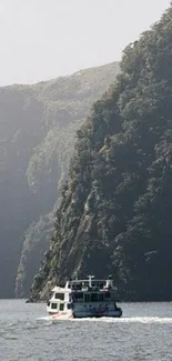 A boat sails on a calm lake surrounded by green mountains under a clear sky.