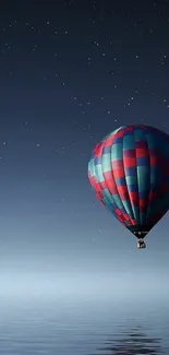 Hot air balloon under a starry night sky, reflecting on water.