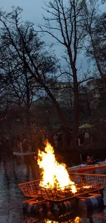 Nighttime bonfire on a tranquil river with dark blue sky.