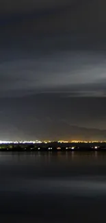 Serene night lake with distant city lights and calm waters.