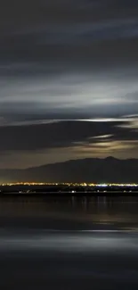 Serene night landscape with calm water reflecting the dark sky and distant lights.