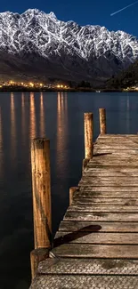 Wooden dock on a lake with mountains under a starry night sky.