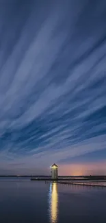 Night sky with clouds over calm water reflecting light and a lone building