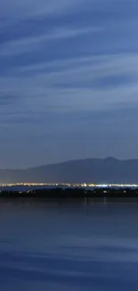 Serene night sky with city lights reflected on a calm blue lake.