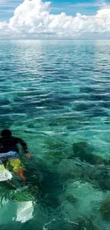 Lone surfer gliding over turquoise ocean under a vast cloudy sky.