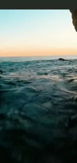 Serene ocean cave view at sunset with calm waters and silhouetted rocks.