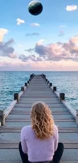 Woman sitting on pier overlooking ocean and sky, serene wallpaper.