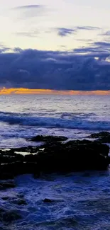 Serene ocean sunset with waves and a rocky shore, under a cloudy sky.