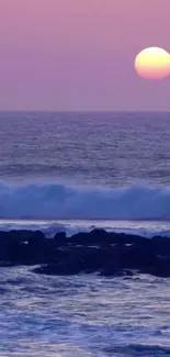 Purple ocean sunset with calm waves and rocky shoreline.