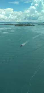 A boat cruising on calm teal ocean with clouds.