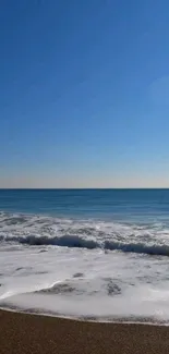 Ocean and beach mobile wallpaper with blue sky and waves.