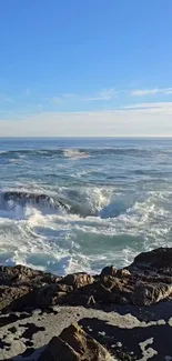 A peaceful ocean view with waves crashing on a rocky shore under a blue sky.