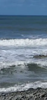 A calming scene of ocean waves on a pebble beach under a clear blue sky.