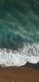 Aerial view of ocean waves hitting the sandy beach with teal and blue hues.