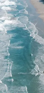 Turquoise ocean waves with white foam on a sandy beach.