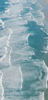 Aerial view of light blue ocean waves on a sandy beach.