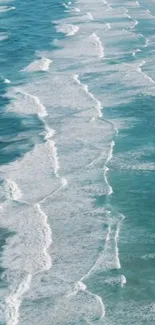 Aerial view of gentle ocean waves with turquoise water on a sandy beach.